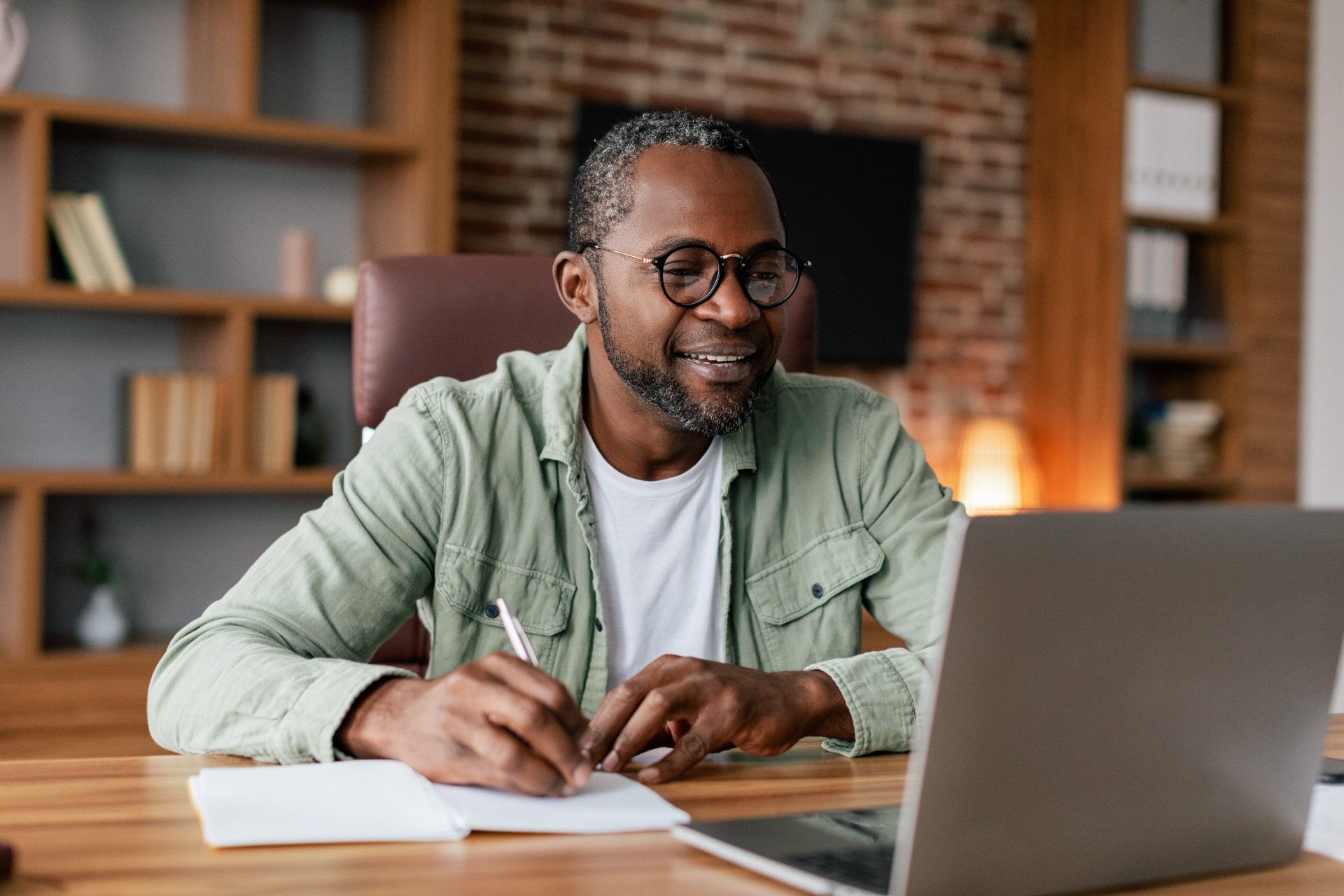 Man in glasses sat at desk with a notebook and laptop